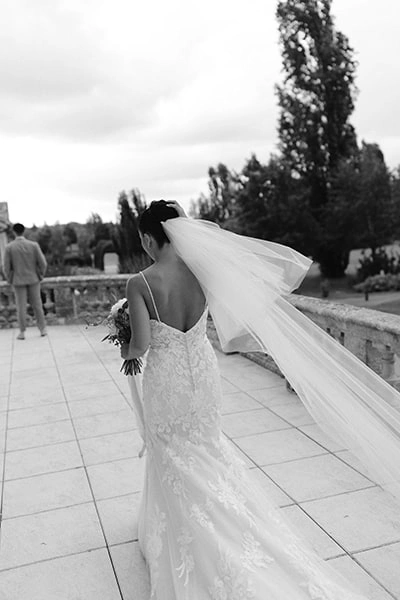 Une mariée de dos va rejoindre le mariée pour la découverte, son voile vol en l'air.