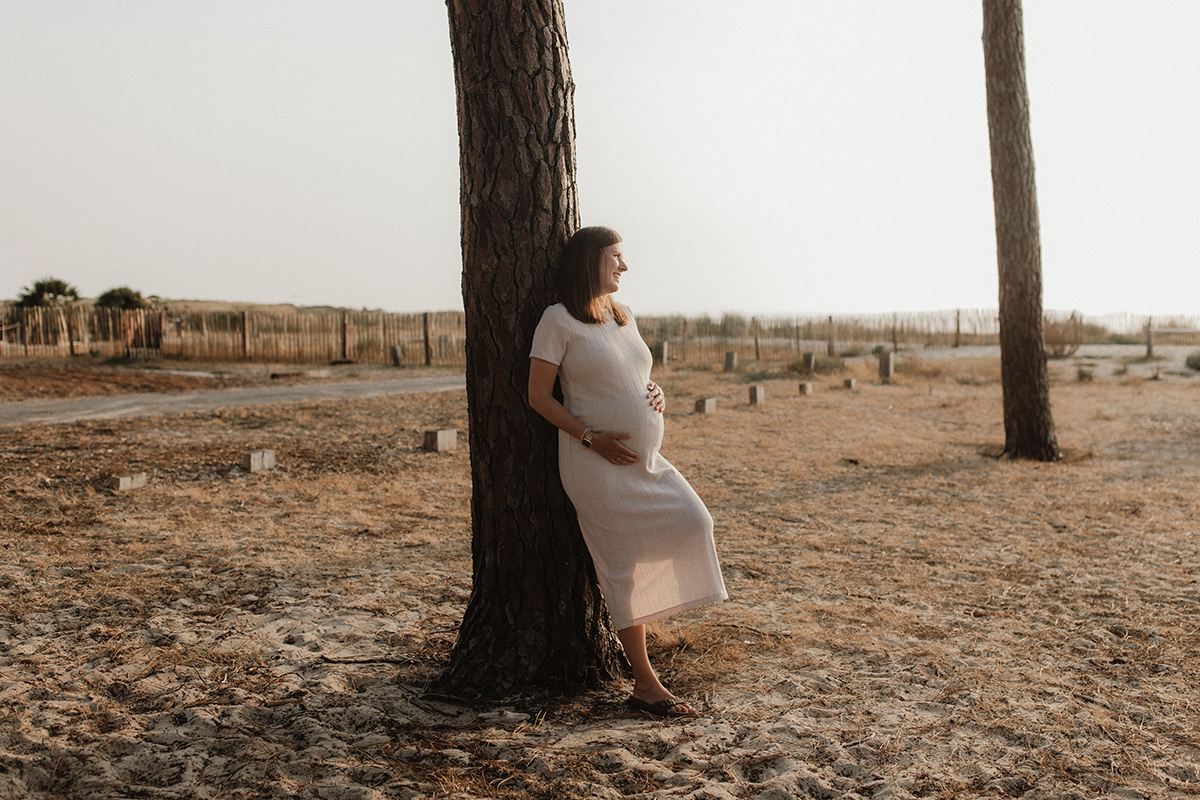 Une femme enceinte debout contre un arbre, ses mains sur son ventre.
