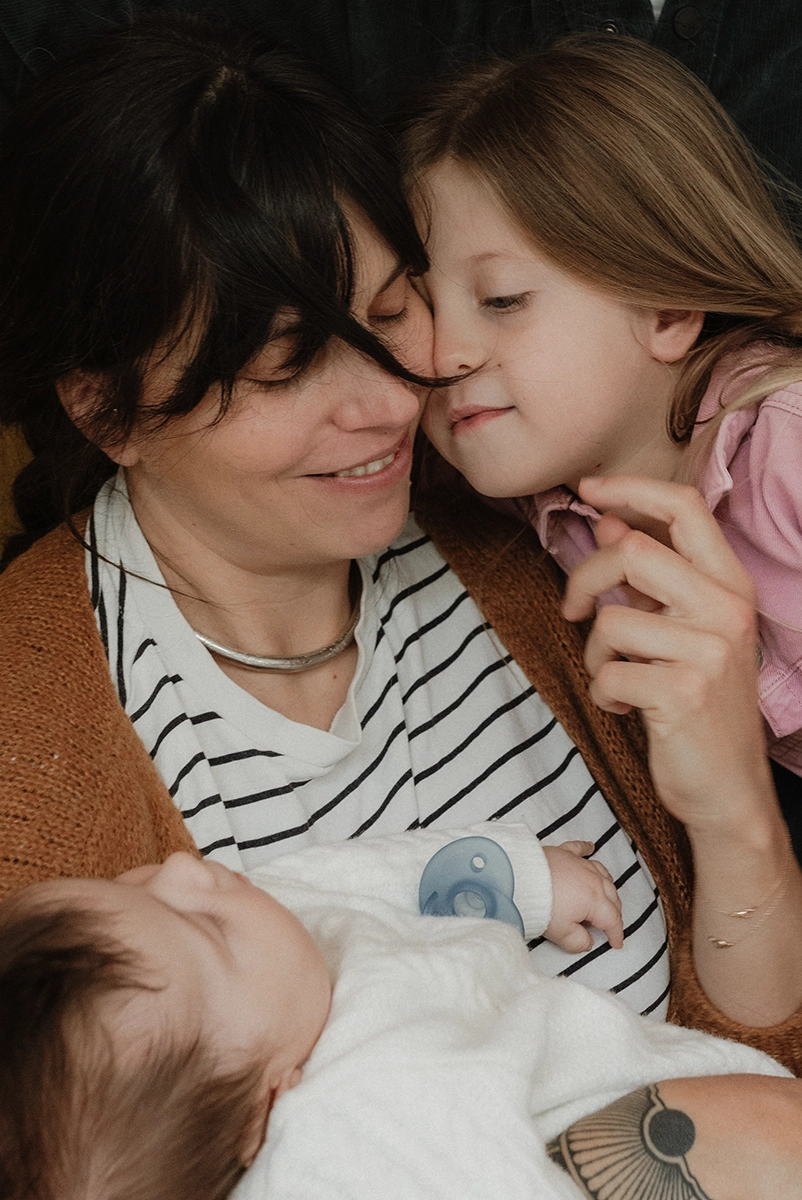 Une mère qui tient dans ses bras son bébé et fait un câlin et son deuxième enfant avec l'autre bras.