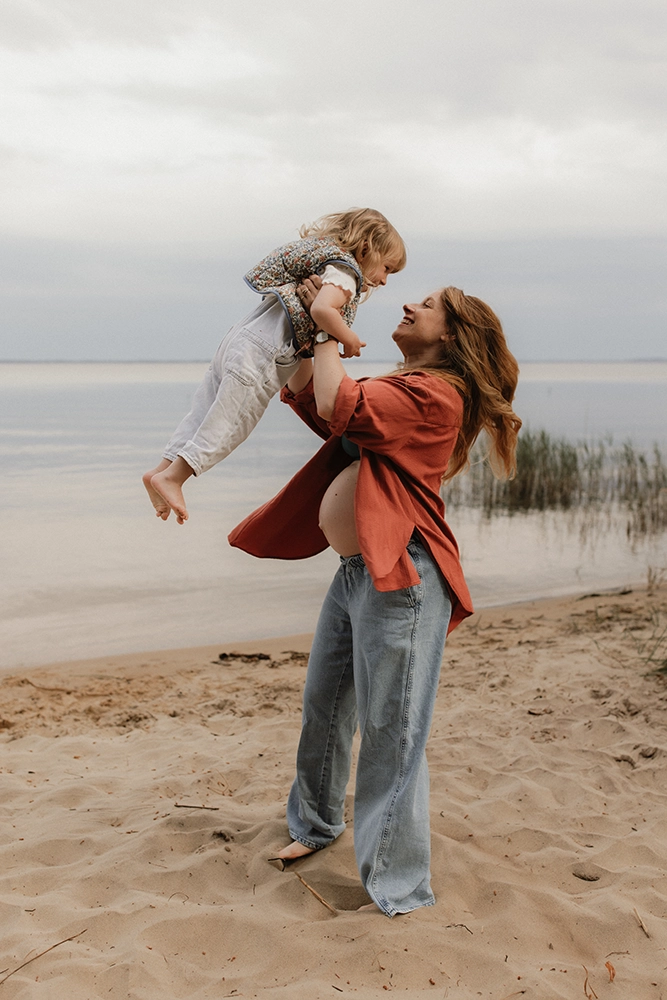 Une mère jour avec sa fille au bord d'un lac en la portant.