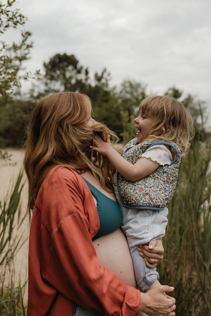 Une petite fille joue avec les cheveux de sa mère qui la porte dans ses bras.