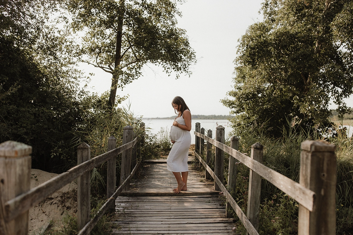 Une femme enceinte sur un petit pont et regarde son ventre.