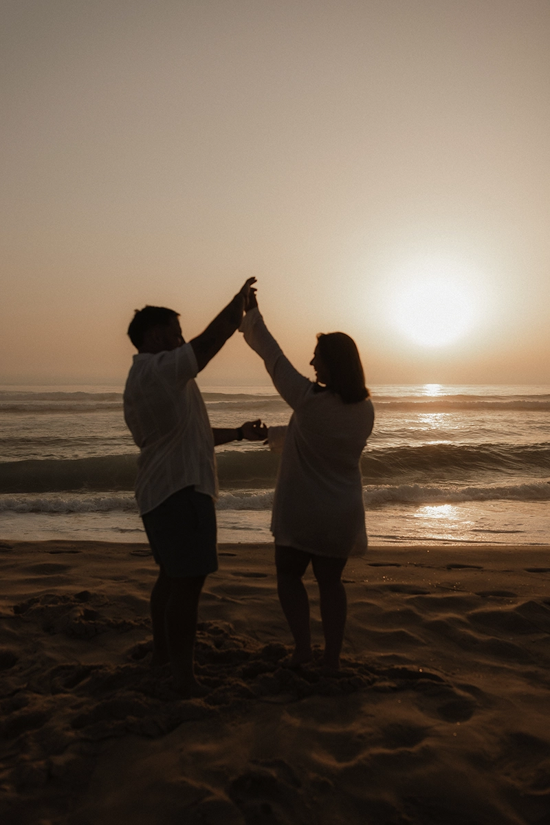 Une couple qui danse à contre jour devant un coucher du soleil à l'océan.