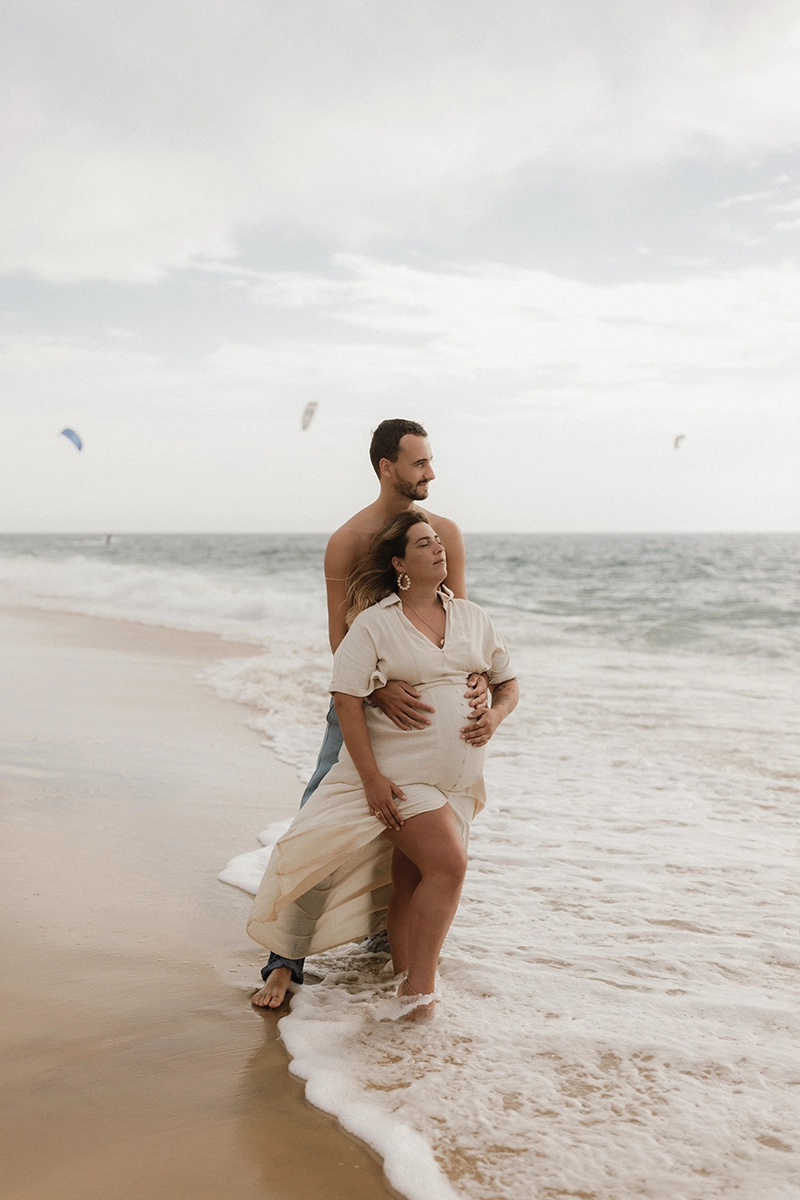Un couple dont la femme est enceinte regardant tous les deux l'océan devant eux.