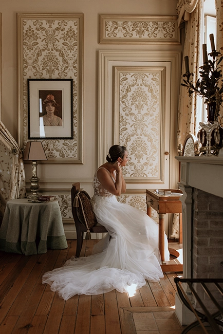 Une mariée se prépare dans sa chambre au château Pape Clément assise sur une jolie chaise.