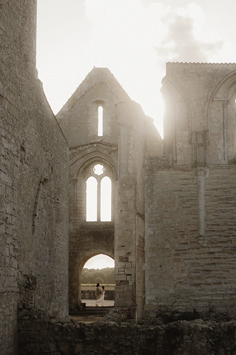 Un couple se tient devant l'entrée d'un abbaye en ruine au coucher du soleil.