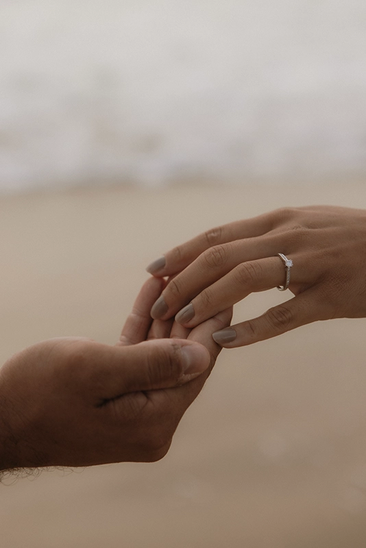Une femme pose délicatement sa main dans celle de son futur mari, on voit sa bague de fiançailles.