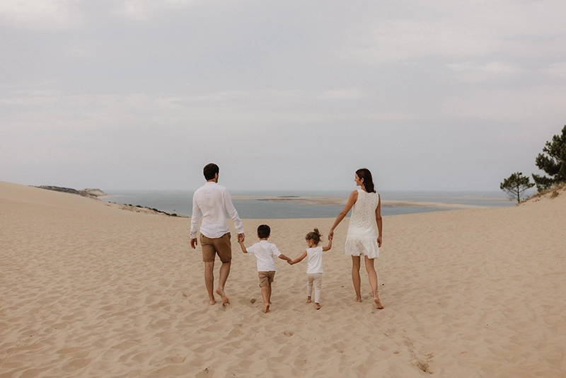 Une famille marche main dans la main sur la dune du Pilat, vers l'océan.