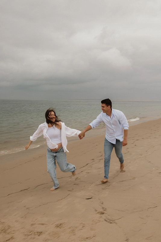 Un jeune couple court au bord de la plage en riant.