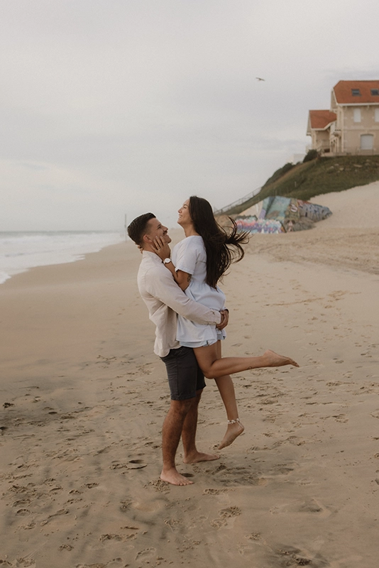 Un homme porte dans ses bras sa femme, les cheveux dans le vent.